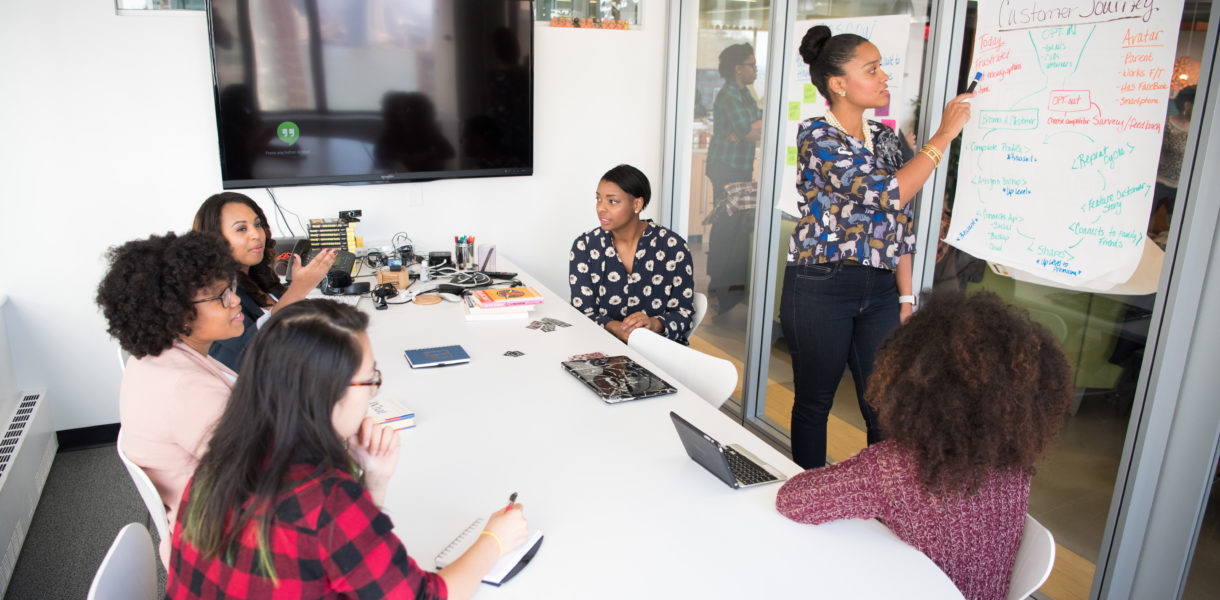 Women in a meeting room discussing and writing a strategy on a whiteboard