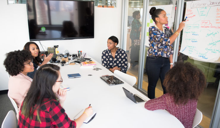 Women in a meeting room discussing and writing a strategy on a whiteboard