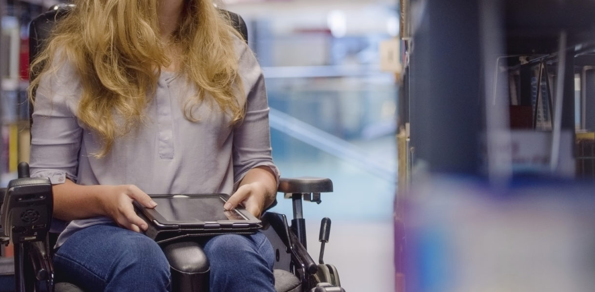 Young woman in wheelchair looking up for book in library and need inclusive design