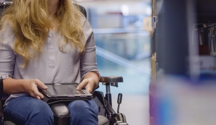 Young woman in wheelchair looking up for book in library and need inclusive design