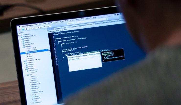 Someone sitting behind a laptop with data and code on their screen