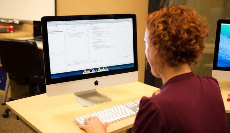 Woman sat at a desk using a Mac Computer to access the internet