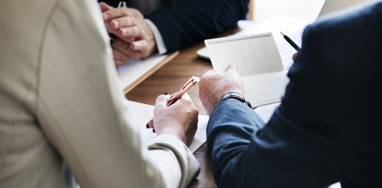 Business people sat in a meeting around a table holding pens, demonstrating Leadership in the Digital Age