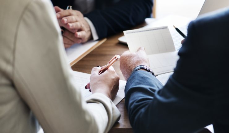 Business people sat in a meeting around a table holding pens, demonstrating Leadership in the Digital Age