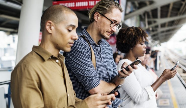 3 people at a train station on their phones