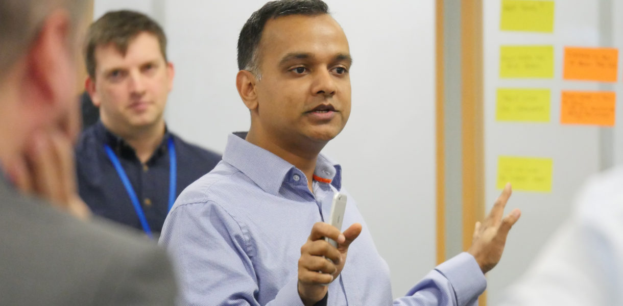 Mayank Prakash talking at a whiteboard with post-it notes on with people in the background