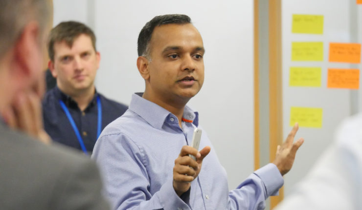 Mayank Prakash talking at a whiteboard with post-it notes on with people in the background