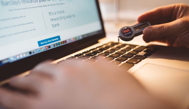 Someone typing at a keyboard whilst holding a security ID fob