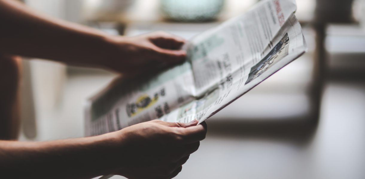 Someone holding a newspaper at arms length and reading the news