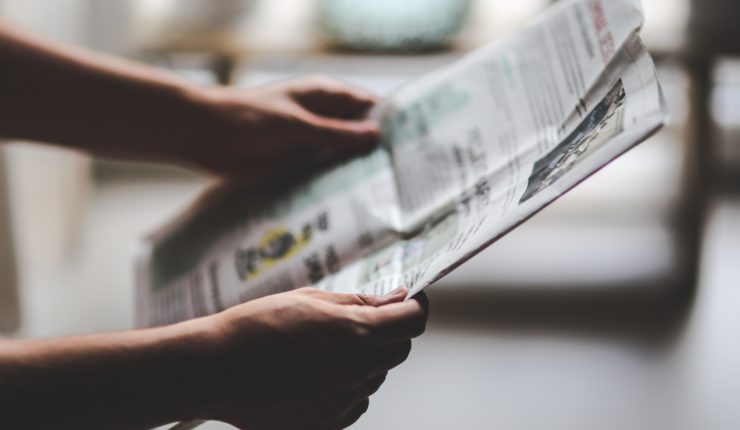 Someone holding a newspaper at arms length and reading the news