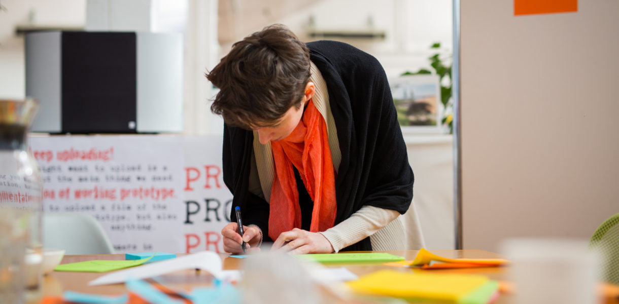 Woman leaning over a table of post-it notes, going through a service design process