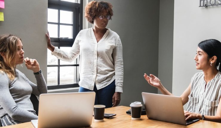 3 women using laptops around a table in a business meeting