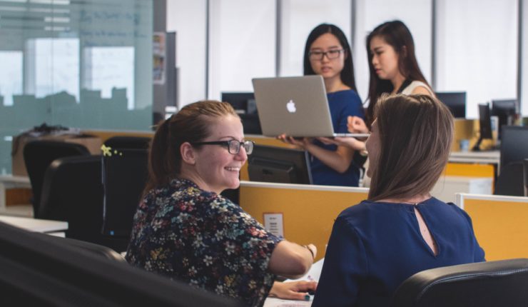 women in office space talking and working on computers