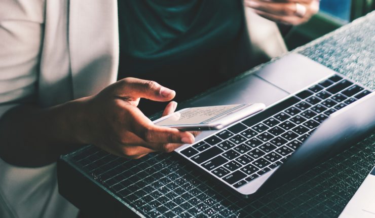 women sitting with computer while typing on phone
