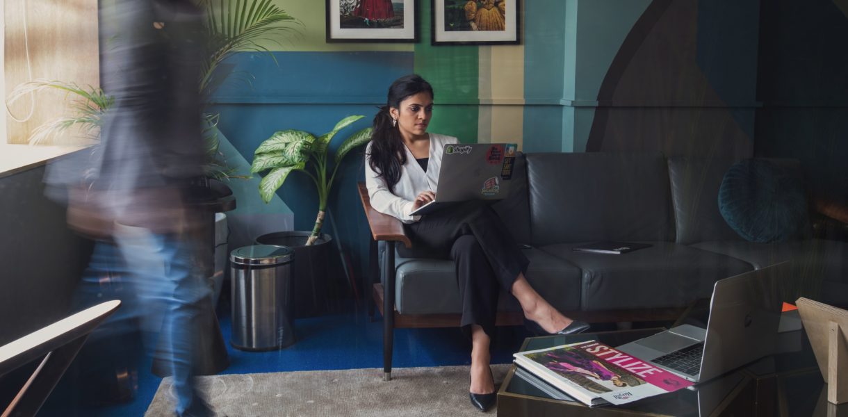 woman sitting on couch with computer while people are walking by her