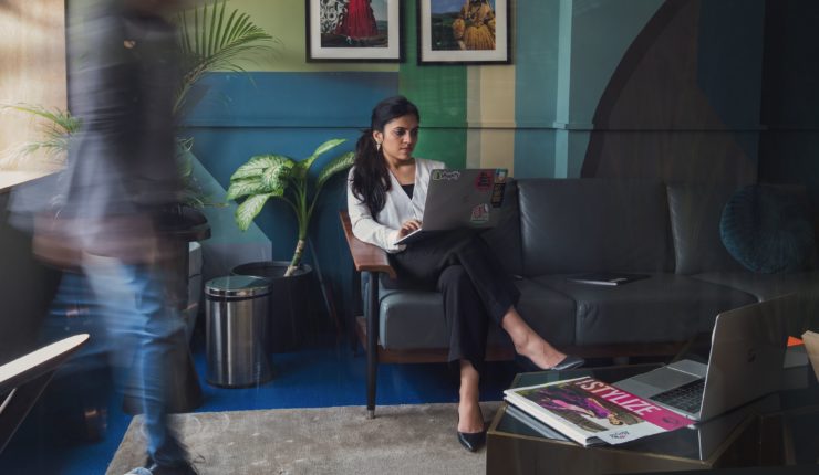 woman sitting on couch with computer while people are walking by her