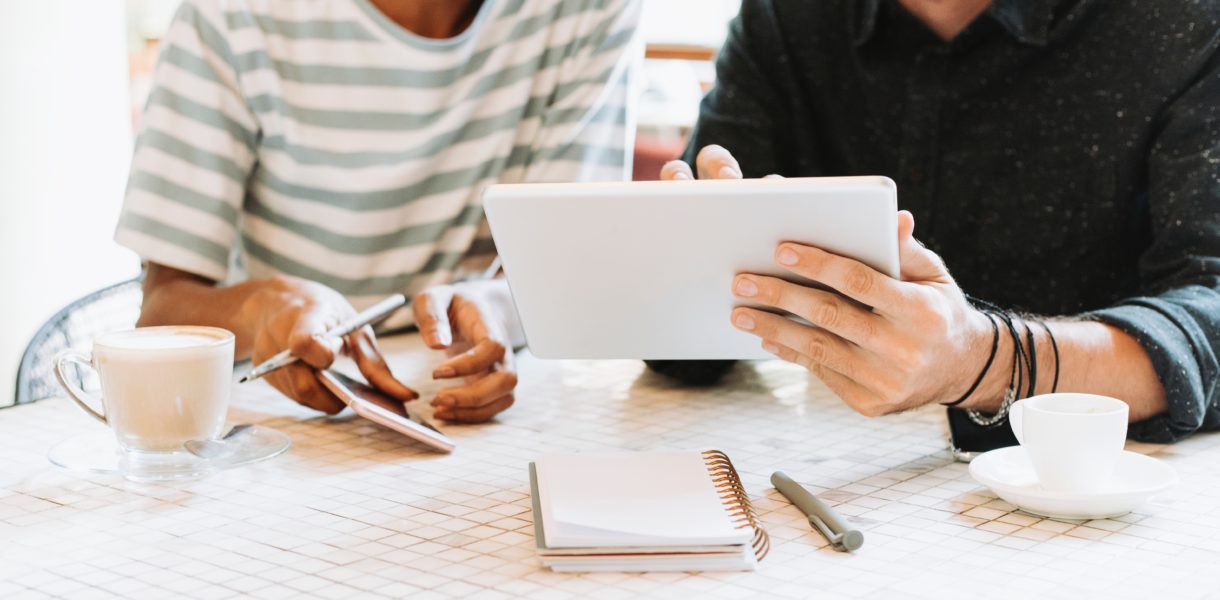 two persons sitting at a desk working on an iPad