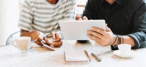 two persons sitting at a desk working on an iPad