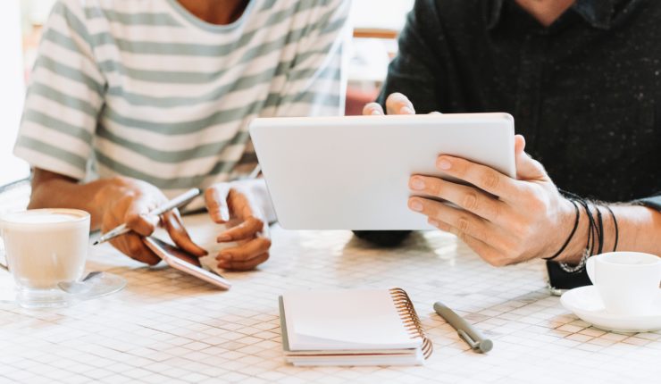 two persons sitting at a desk working on an iPad