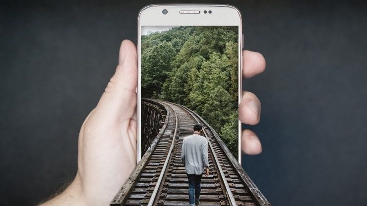 Man wlaking on traintrack on a photo displayed on iPhone (The image come out of the phone)