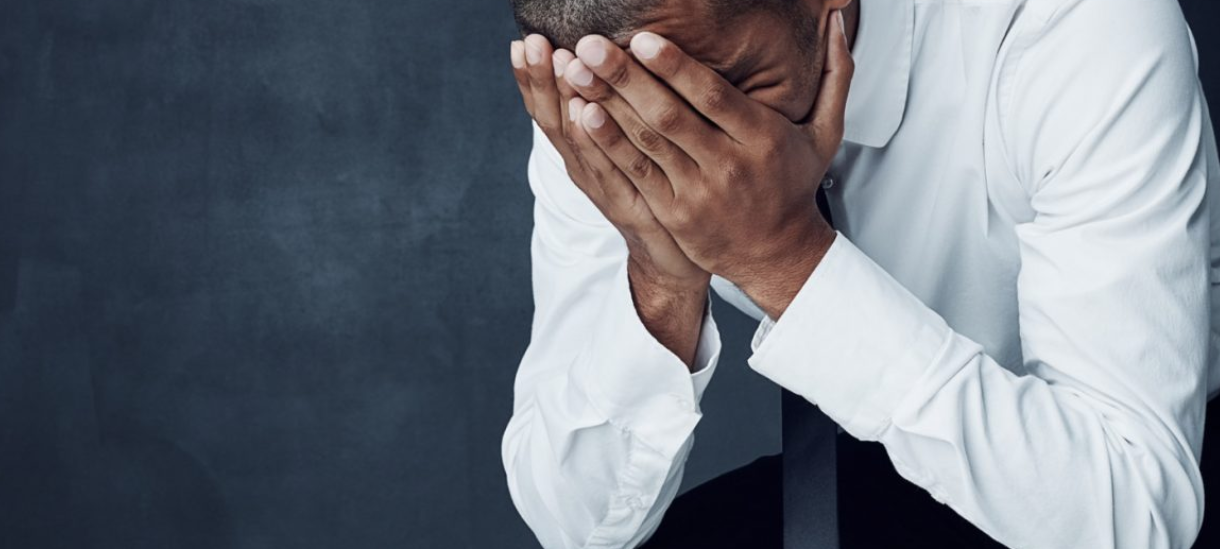Man bend over holding his face in his hands