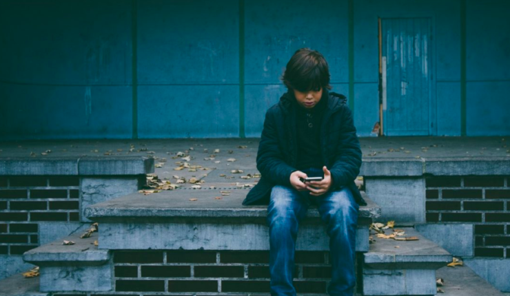 young boy using phone, sitting outside