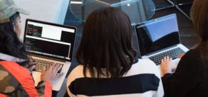Three women sitting on a couch with computers