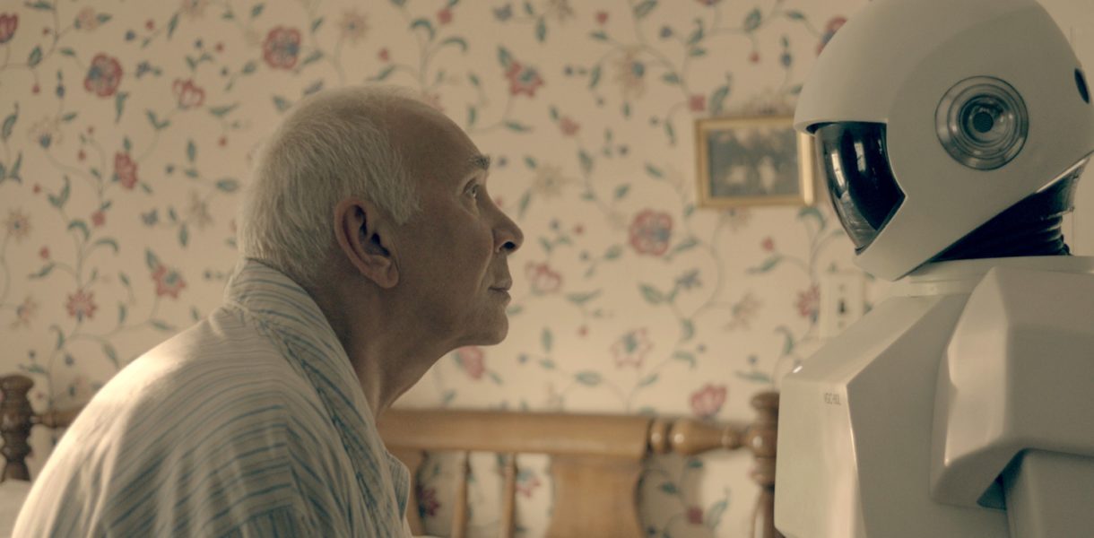 Elderly man sitting in bed looking at human sized robot