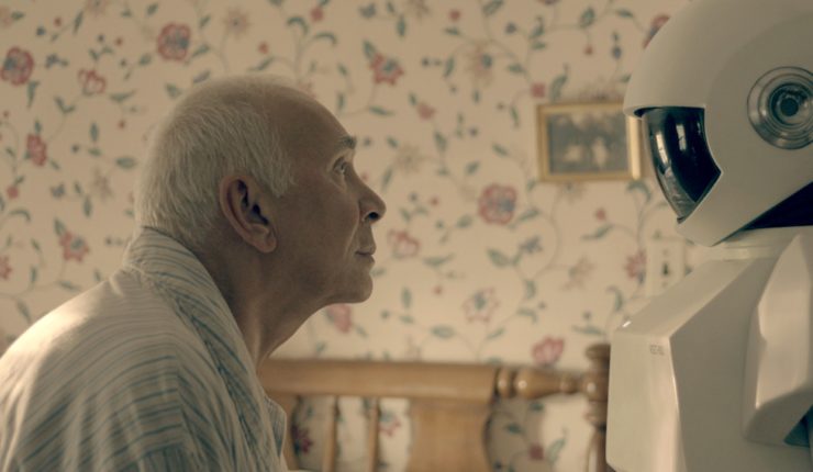 Elderly man sitting in bed looking at human sized robot