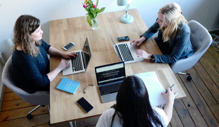 three women sitting at desk with computers
