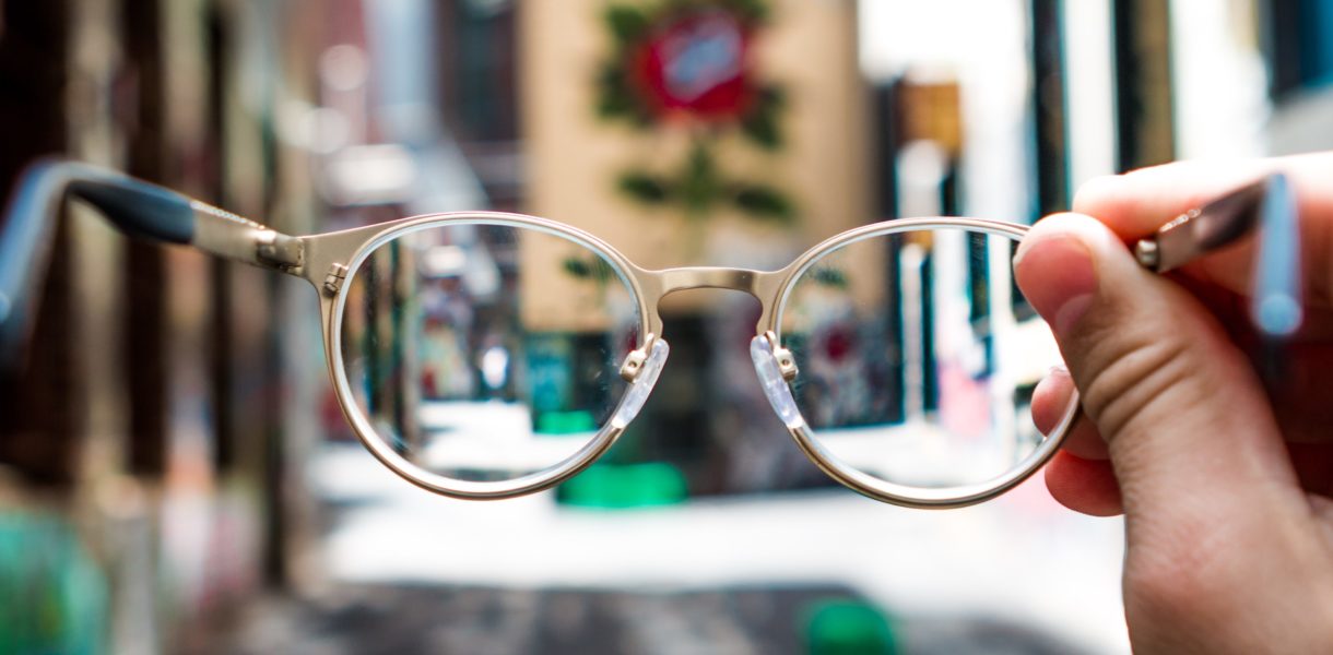 pair of glasses held in front of person on the street
