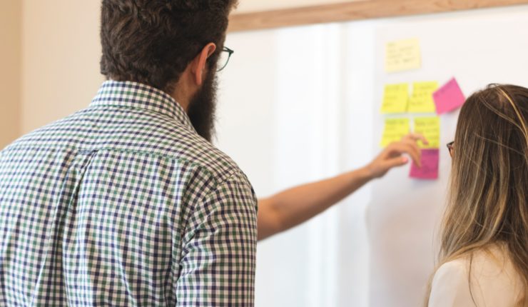 man and woman putting post t notes on whiteboard