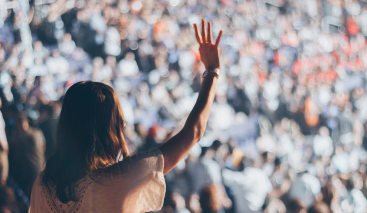 woman standing up in crowd, raising her hand