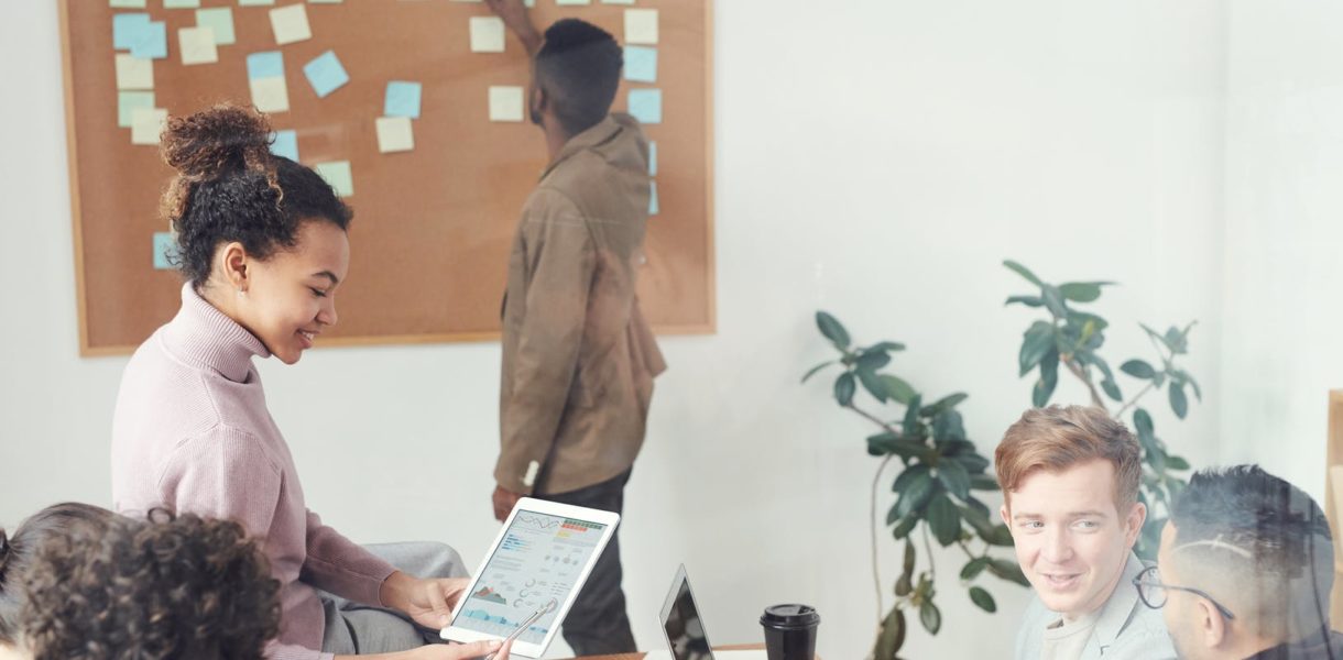 Group meeting at office, man in the background putting up post it notes