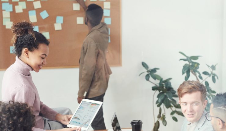 Group meeting at office, man in the background putting up post it notes