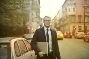 Male carrying laptop next to cars in the street