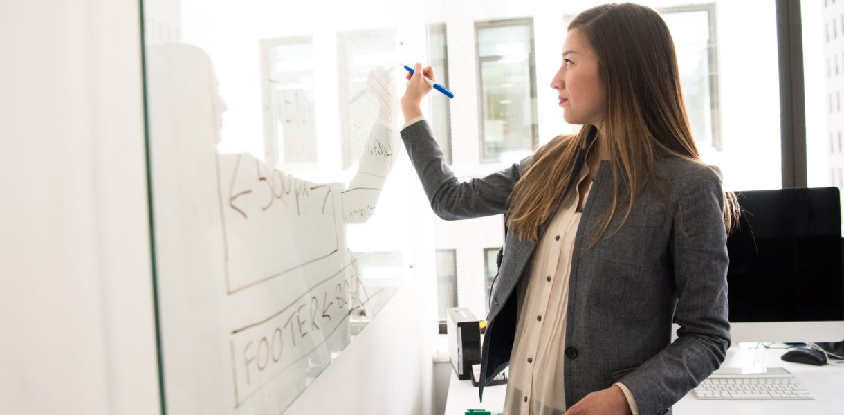 woman in grey blazer writing on a whiteboard
