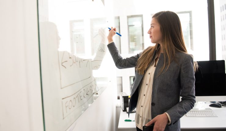 woman in grey blazer writing on a whiteboard