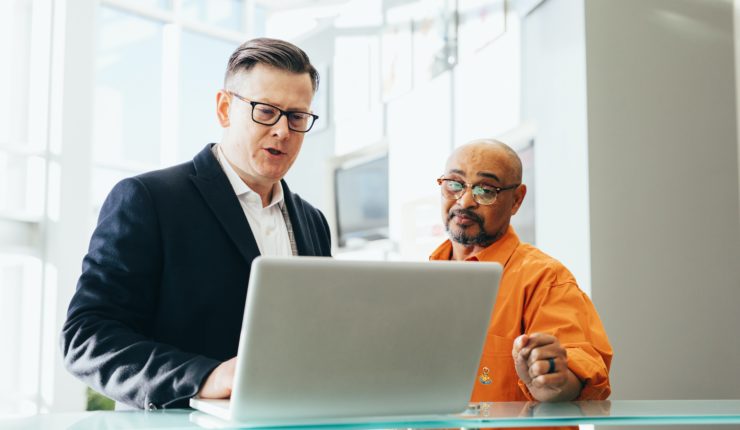 two men talking at table looking at a laptop