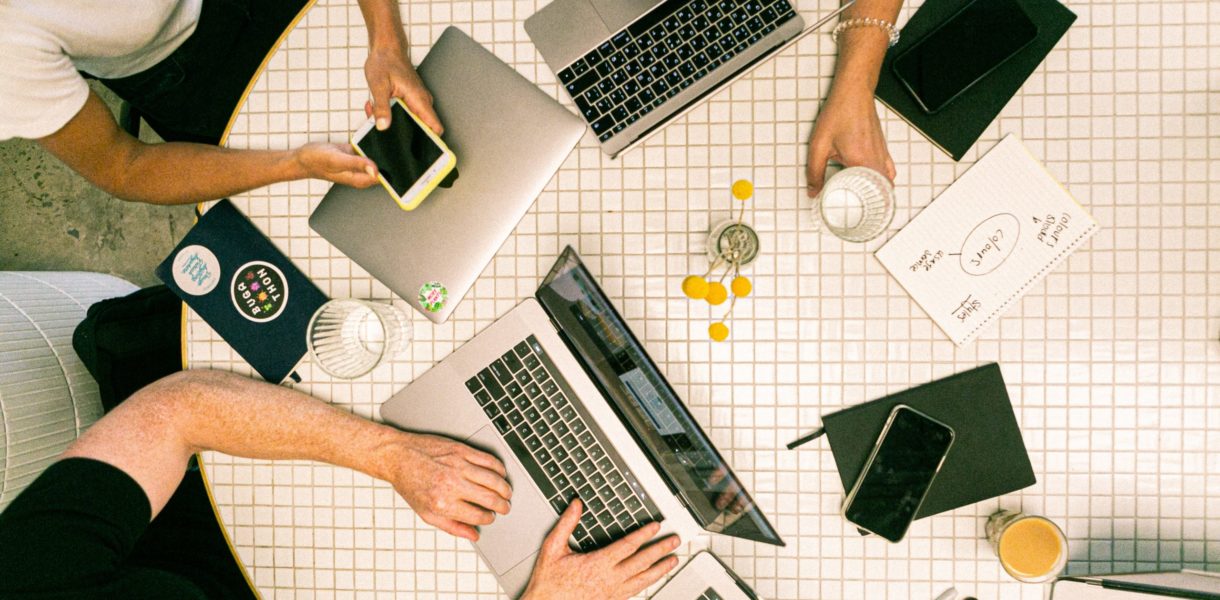 Group of people working round a table on laptops and phones