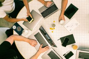 Group of people working round a table on laptops and phones