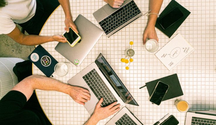 Group of people working round a table on laptops and phones