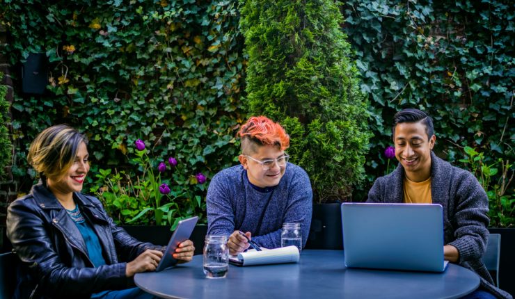 Woman and 2 men working at a table round a laptop