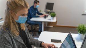 Man and woman in mask using laptops