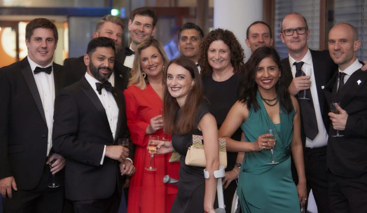 Attendees of the DL100 Awards event gathered around in black tie, smiling at the camera