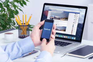 Man using facabook on laptop and phone