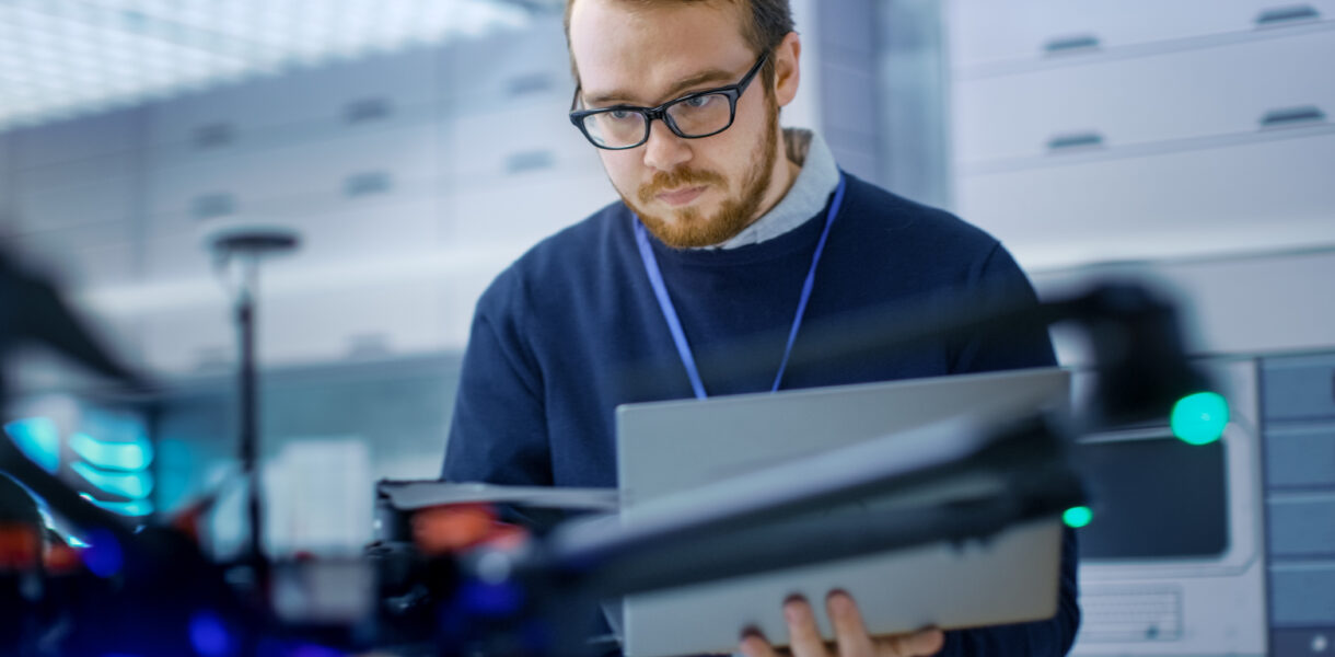 Young,Male,Engineer,Programs,Drone,While,Holding,Laptop,In,His