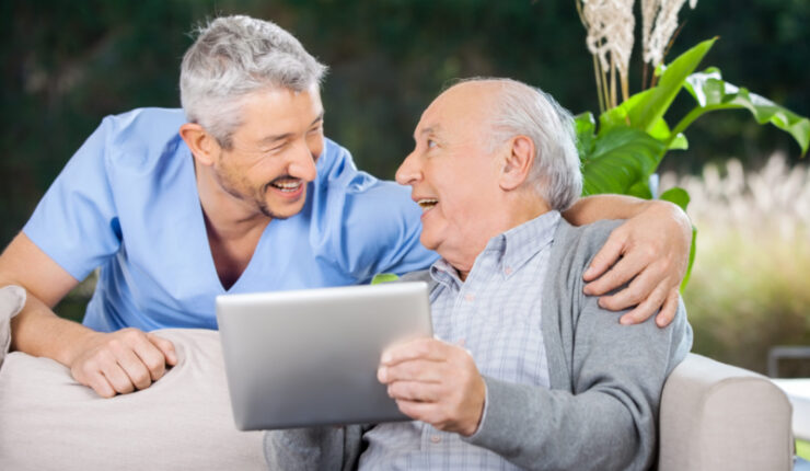 Laughing,Male,Caretaker,And,Senior,Man,Using,Tablet,Computer,At